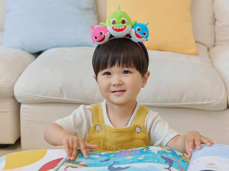 Child wearing the Baby Shark Squishy Charm Plush headband while looking at a picture book