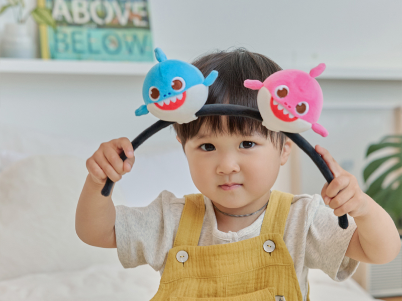 Child holding up the Baby Shark Squishy Charm Plush headband with both hands
